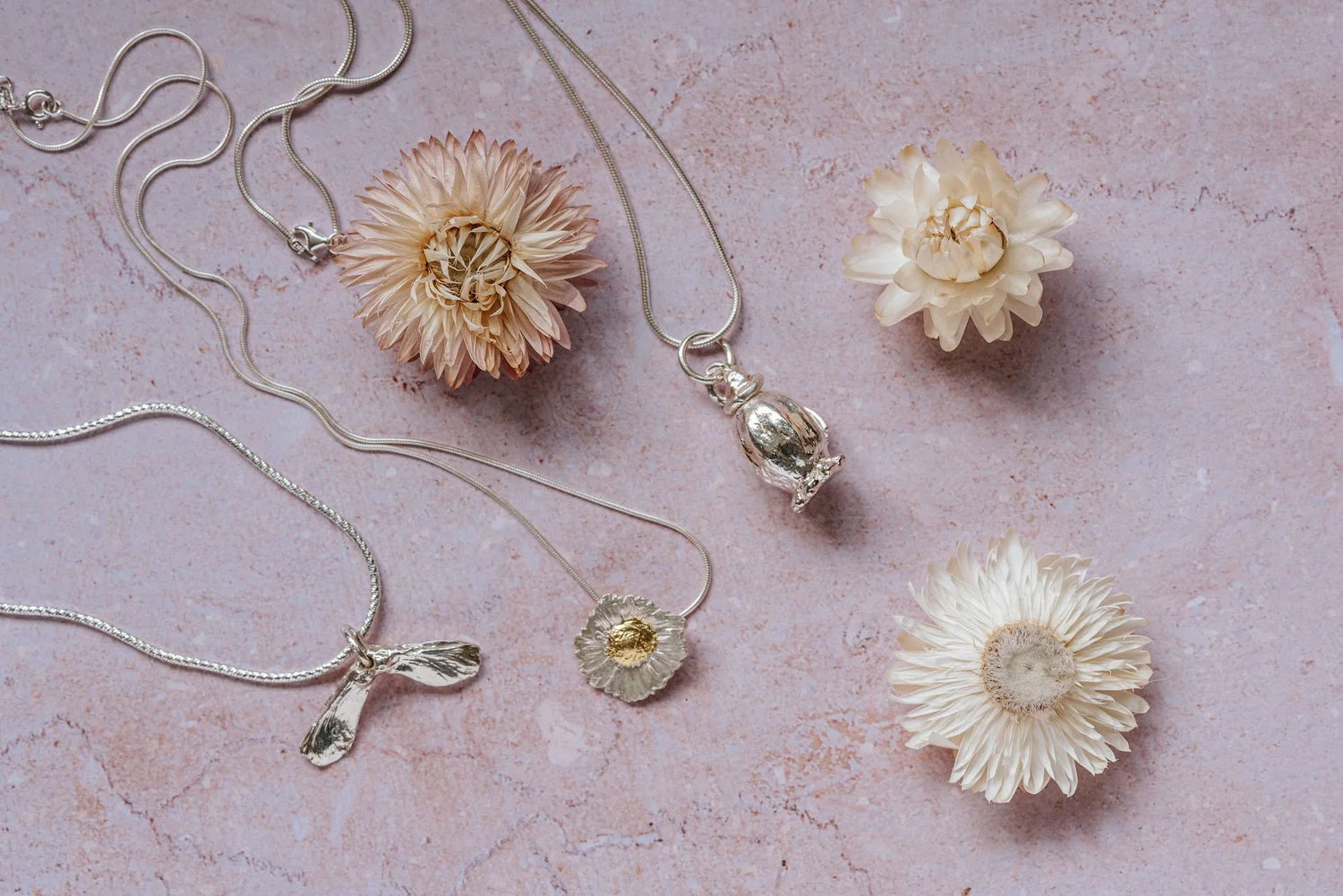 flatlay of silver daisy pendant necklace with gold-leaf centre on sterling silver chain with dried flowers