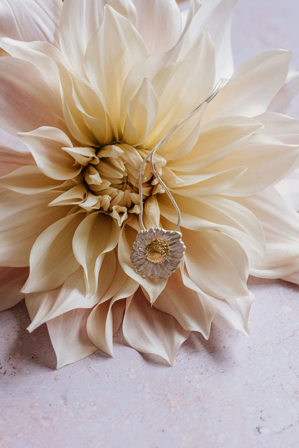 silver daisy pendant necklace with gold-leaf centre displayed on cream dahlia flower
