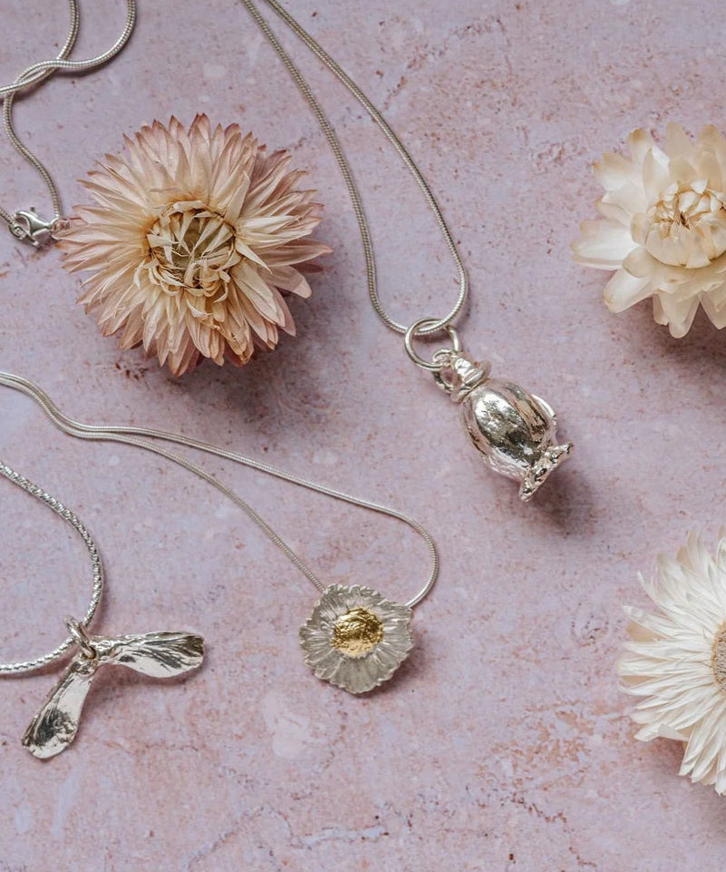 Poppy seedhead silver pendant necklace styled with other botanical silver jewellery and dried flowers