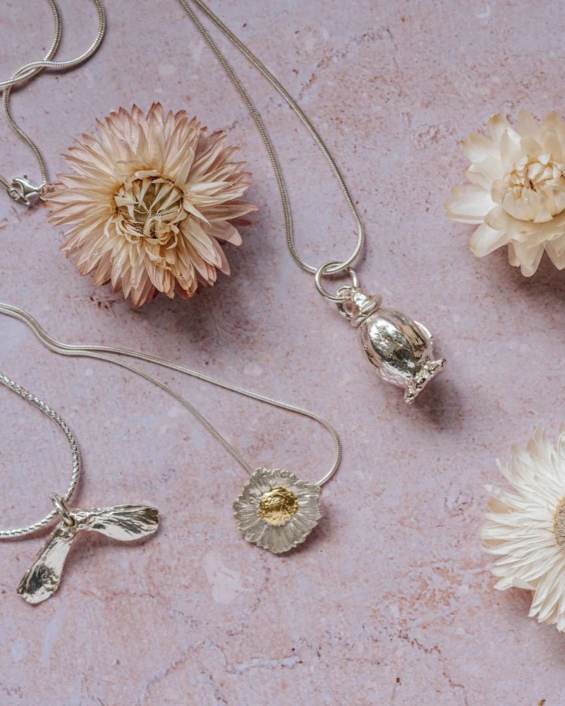 Poppy seedhead silver pendant necklace styled with other botanical silver jewellery and dried flowers