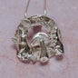 Close-up of silver rabbits and mushroom necklace pendant with two rabbits and a central mushroom, set against a soft pink background