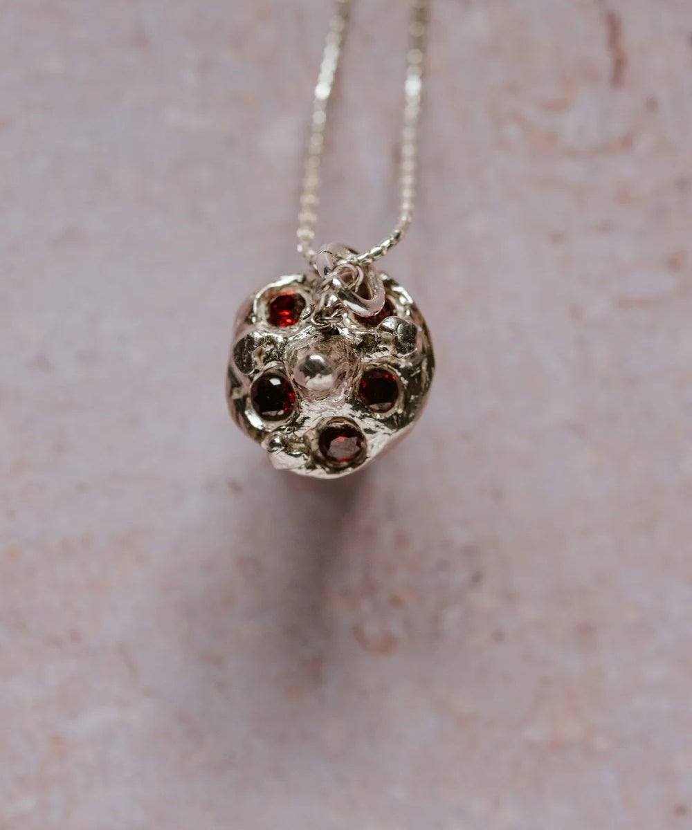 top view of silver toadstool mushroom pendant with red cubic zirconia gemstones, hanging on a chain against a soft textured background