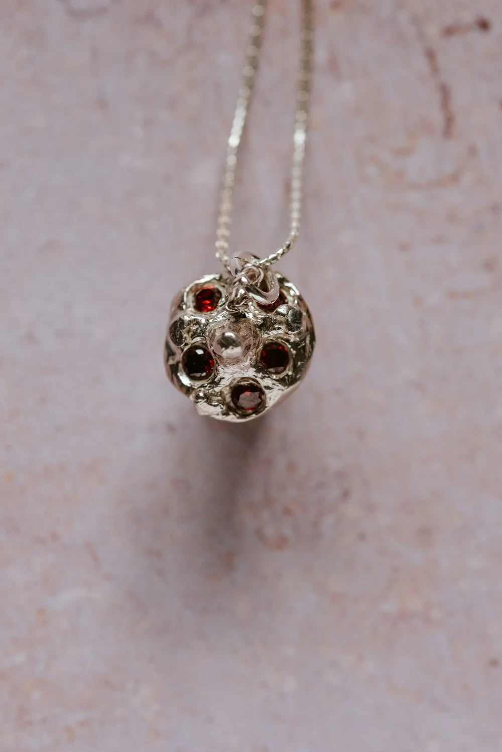 top view of silver toadstool mushroom pendant with red cubic zirconia gemstones, hanging on a chain against a soft textured background
