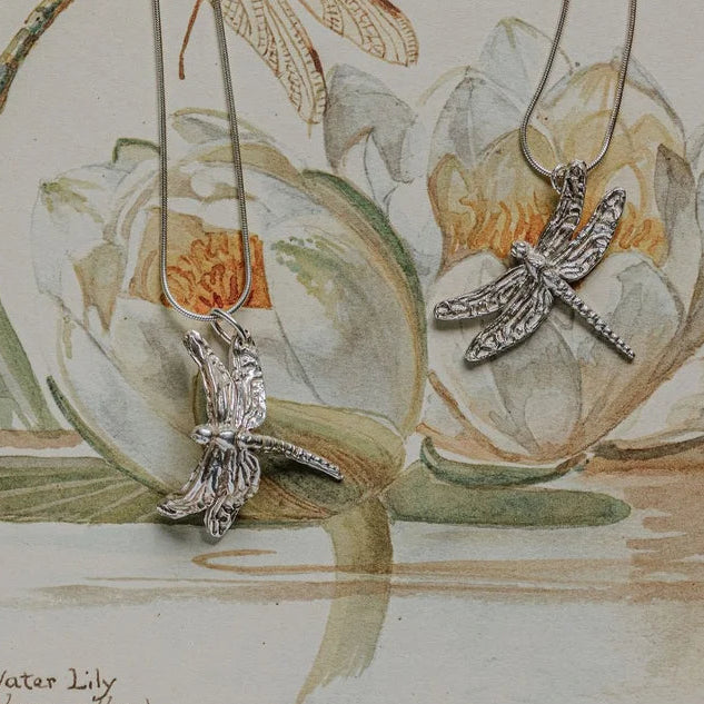 Handmade silver dragonfly necklaces displayed on vintage botanical illustration, symbolic artisan jewellery gift UK