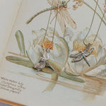 Dragonfly Necklace 3 in fine silver displayed on vintage botanical book with dragonfly illustration, artisan nature inspired jewellery gift UK