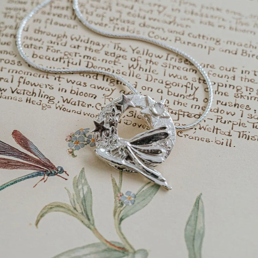 Handmade silver dragonfly and stars pendant necklace with moonstone cabochon displayed on vintage botanical book, artisan celestial jewellery gift for her UK