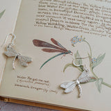Handcrafted silver dragonfly earrings resting on vintage botanical book page with water forget-me-not illustration.