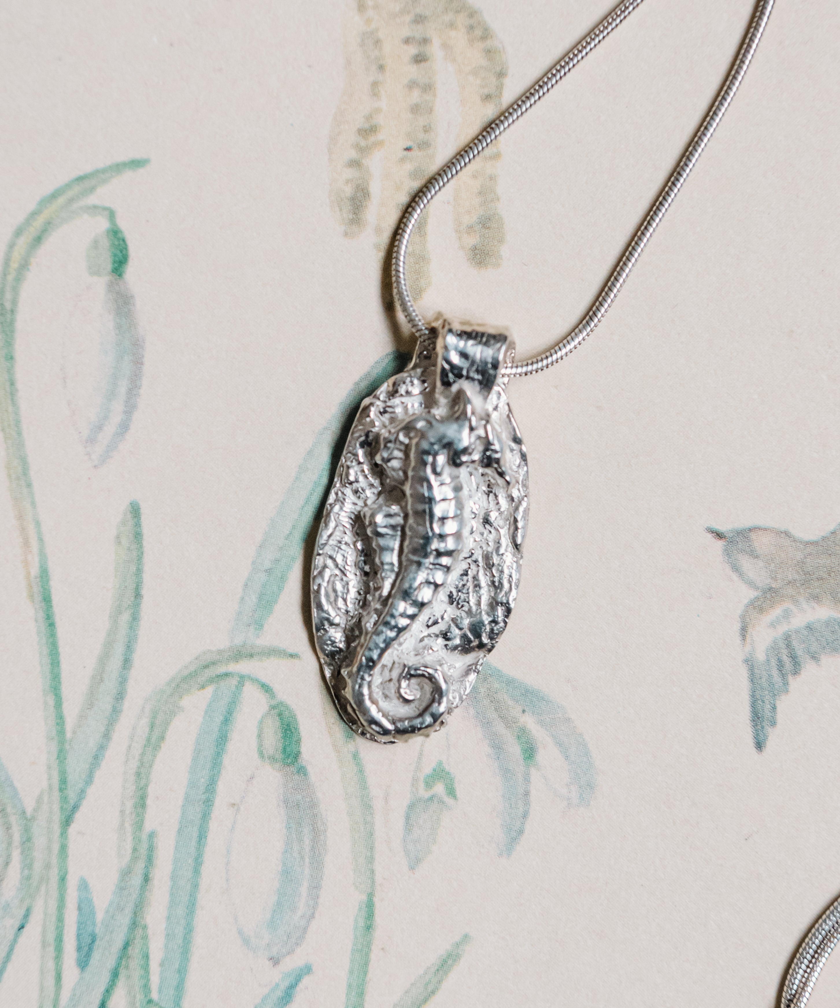 Handmade sterling silver seahorse pendant necklace inspired by ocean life on illustrated background