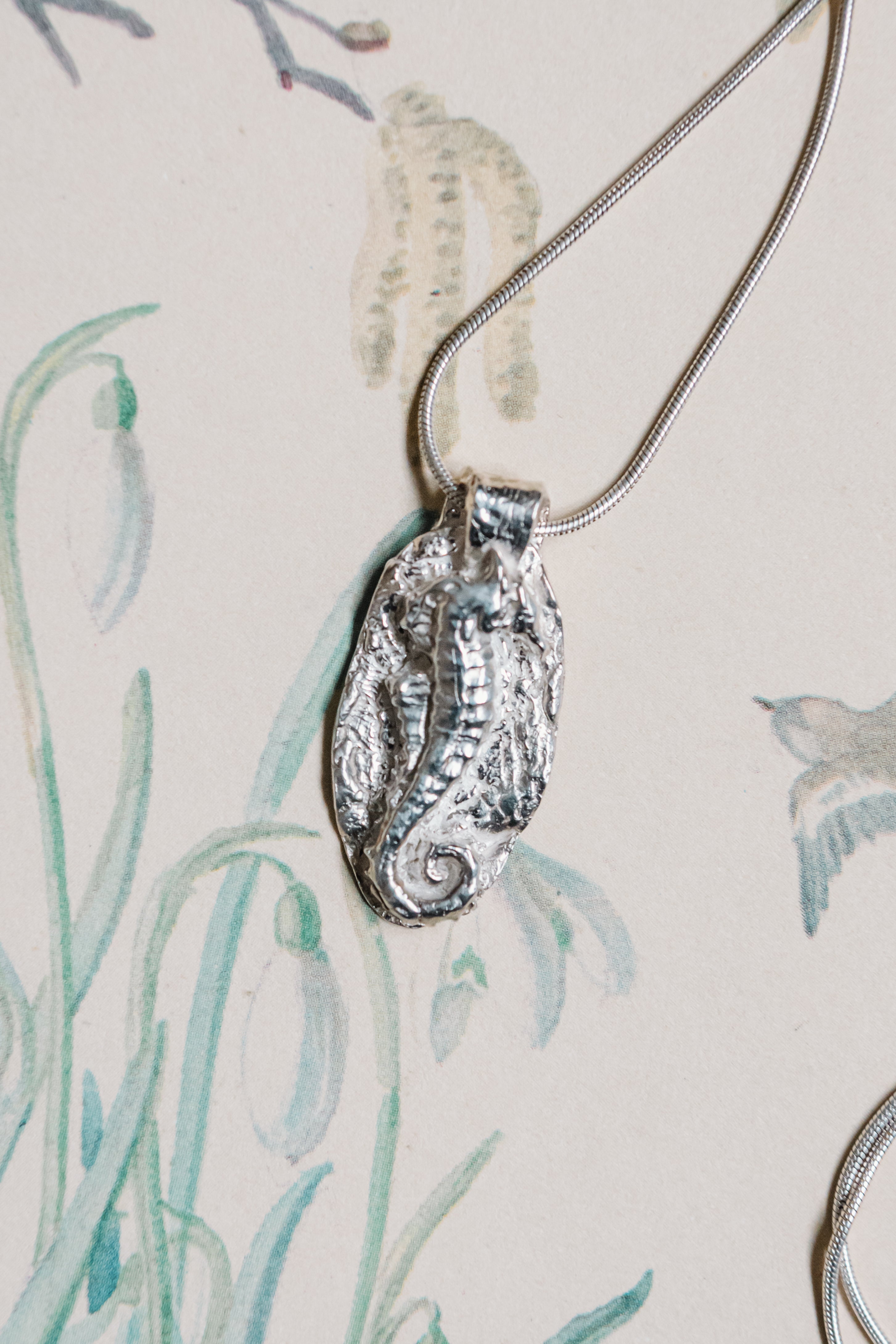 Handmade sterling silver seahorse pendant necklace inspired by ocean life on illustrated background