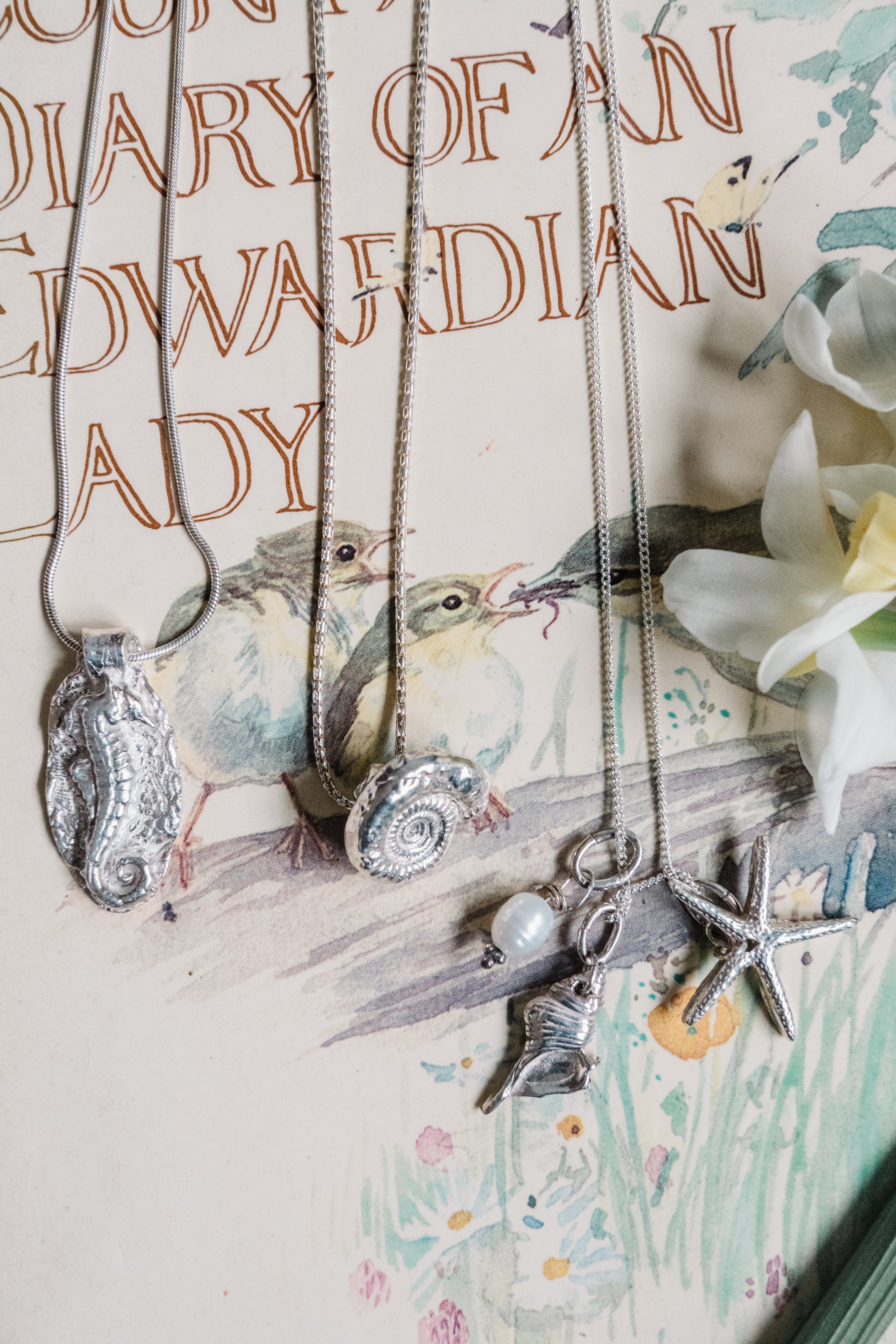Handmade sterling silver ocean inspired pendant necklaces with seahorse, shell, starfish and pearl charms on illustrated background