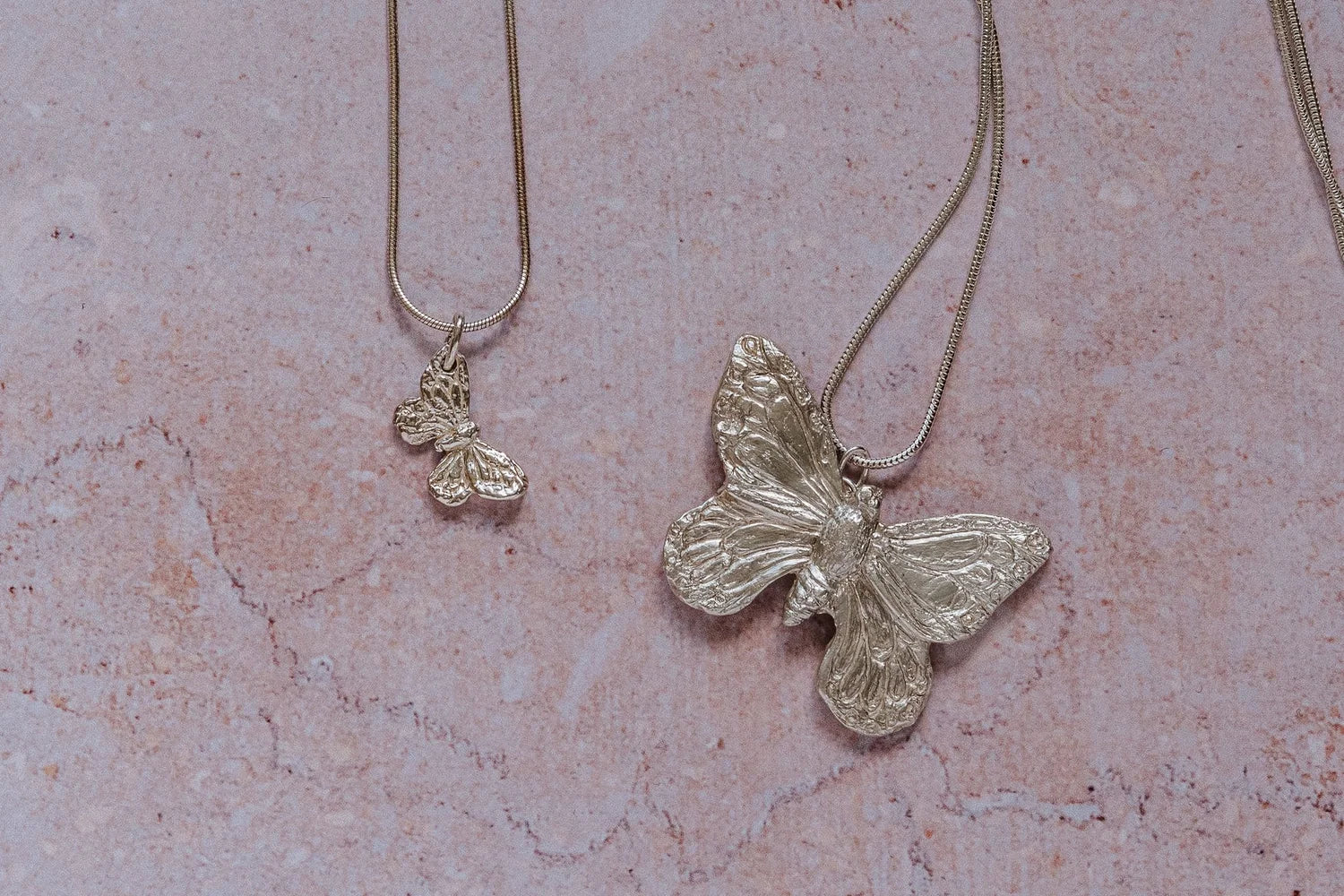 Handmade recycled silver large butterfly pendant and small butterfly pendant on 18-inch snake chains, displayed on textured stone background