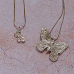 Handmade recycled silver large butterfly pendant and small butterfly pendant on 18-inch snake chains, displayed on textured stone background