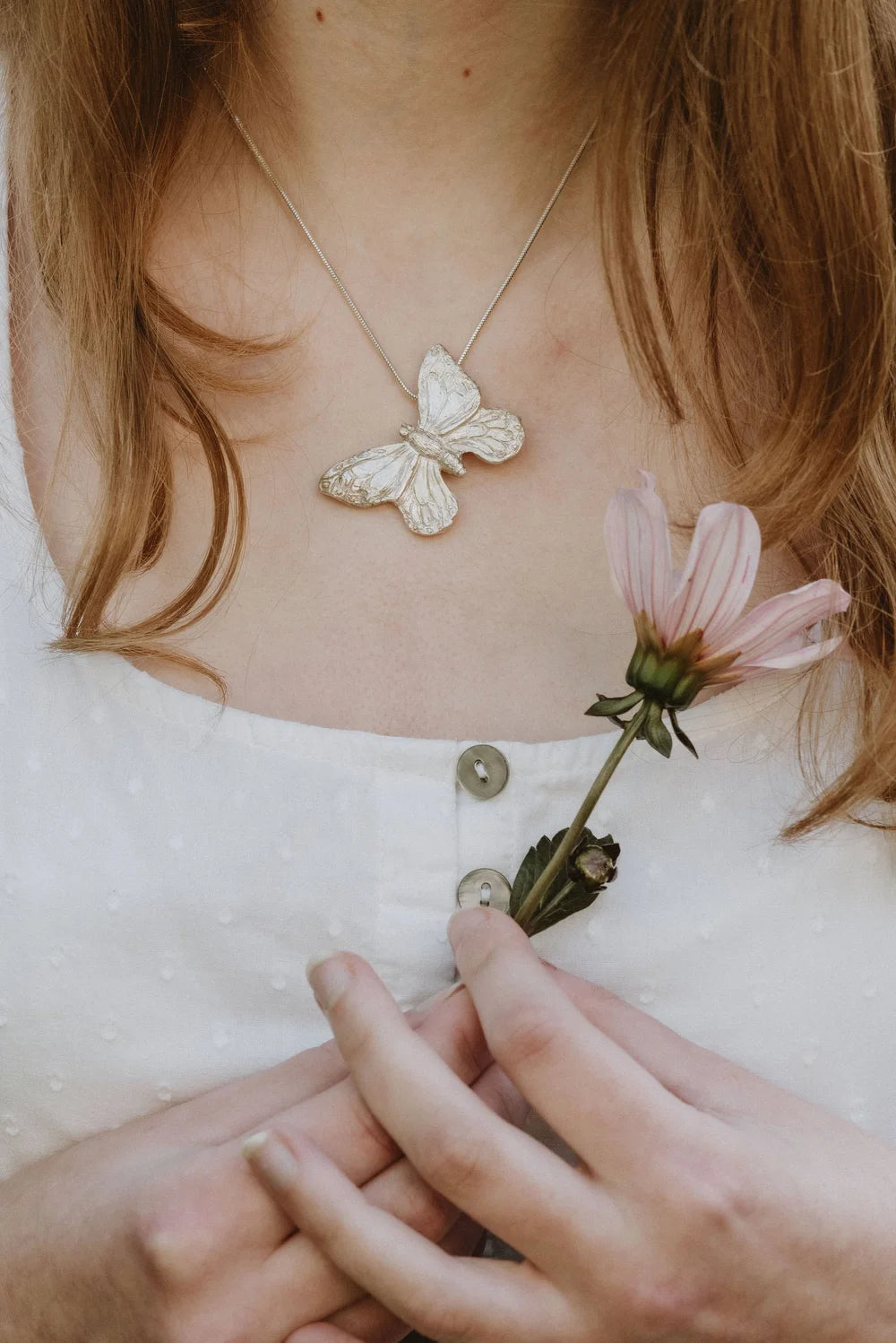 Large silver butterfly pendant worn on snake chain, model holding pink flower