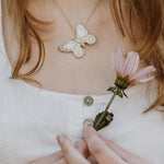 Large silver butterfly pendant worn on snake chain, model holding pink flower