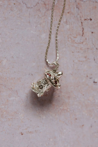Angled close-up of handmade silver mushroom toadstool necklace with red cubic zirconia stones, displayed on pink background

