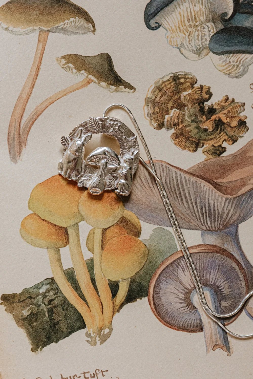 Handmade silver pendant with two rabbits and a mushroom styled on a vintage illustration of yellow and brown woodland fungi