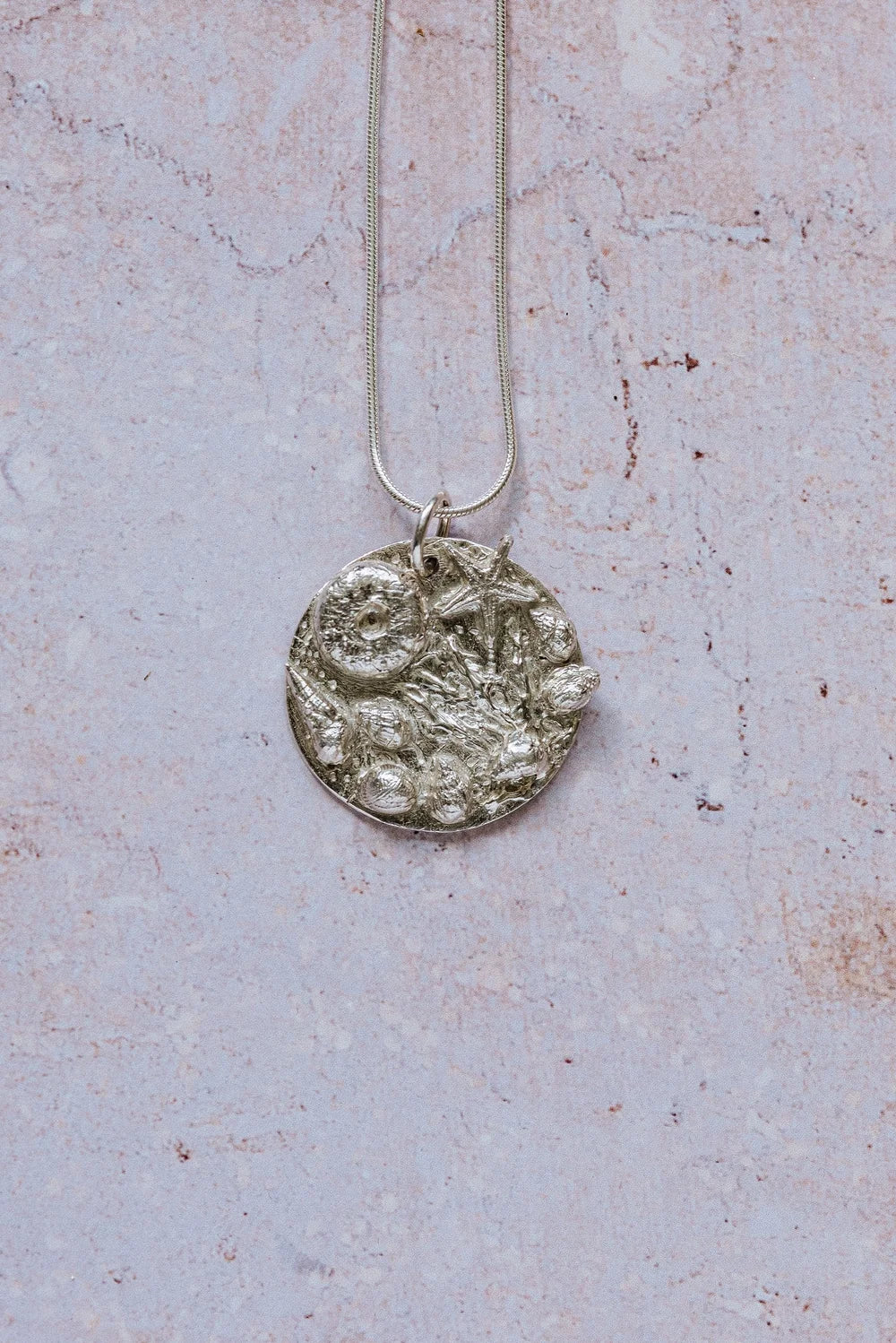 Handmade recycled silver rockpool pendant with starfish and shells on 16-inch chain, displayed on textured stone background