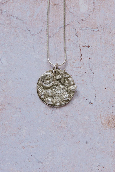 Handmade recycled silver rockpool pendant with starfish and shells on 16-inch chain, displayed on textured stone background