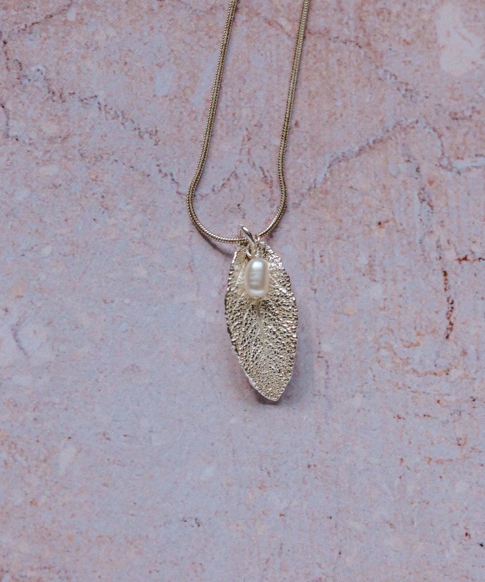 Silver sage leaf pendant with a pearl on a chain against a pink marble background