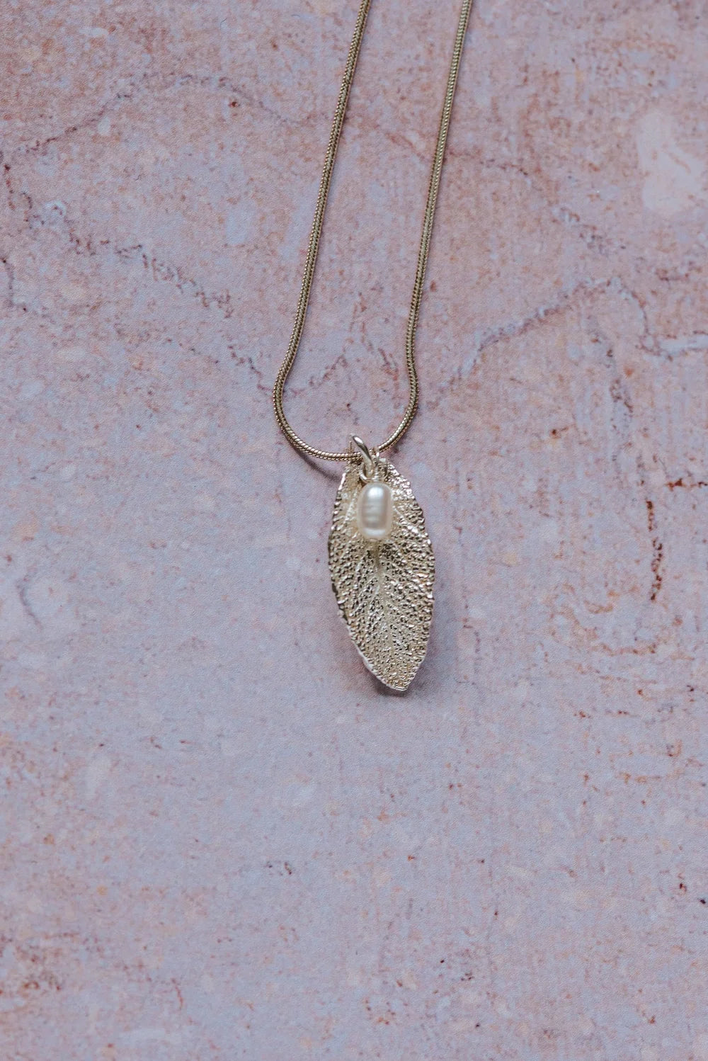 Silver sage leaf pendant with a pearl on a chain against a pink marble background