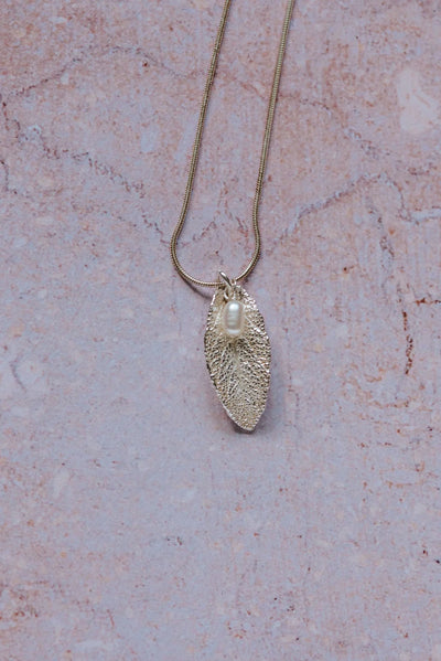 Silver sage leaf pendant with a pearl on a chain against a pink marble background