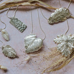 Silver botanical pendant necklaces styled with dried grasses and natural props, showcasing a soft, nature-inspired collection.