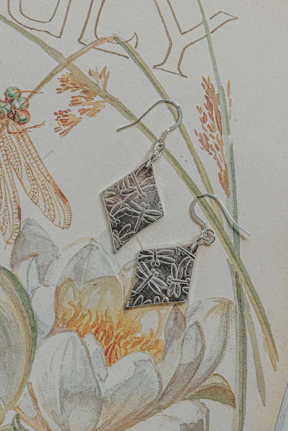 a pair of fine silver earrings with a fun dragonfly impression and a unique diamond shape 