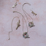 Flat lay of handmade silver dragonfly jewellery collection on pink background, including dragonfly earrings, moon dragonfly pendants, and catkin dragonfly pendant, artisan nature inspired jewellery gifts UK