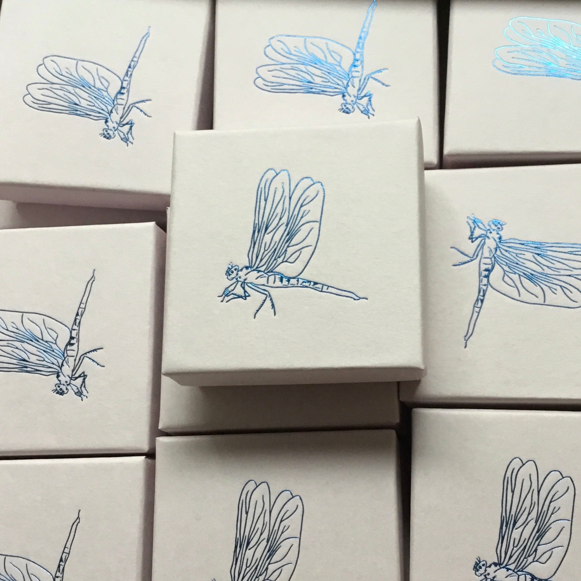 Stack of white jewellery gift boxes decorated with delicate blue dragonfly illustrations, packaging for handmade silver jewellery