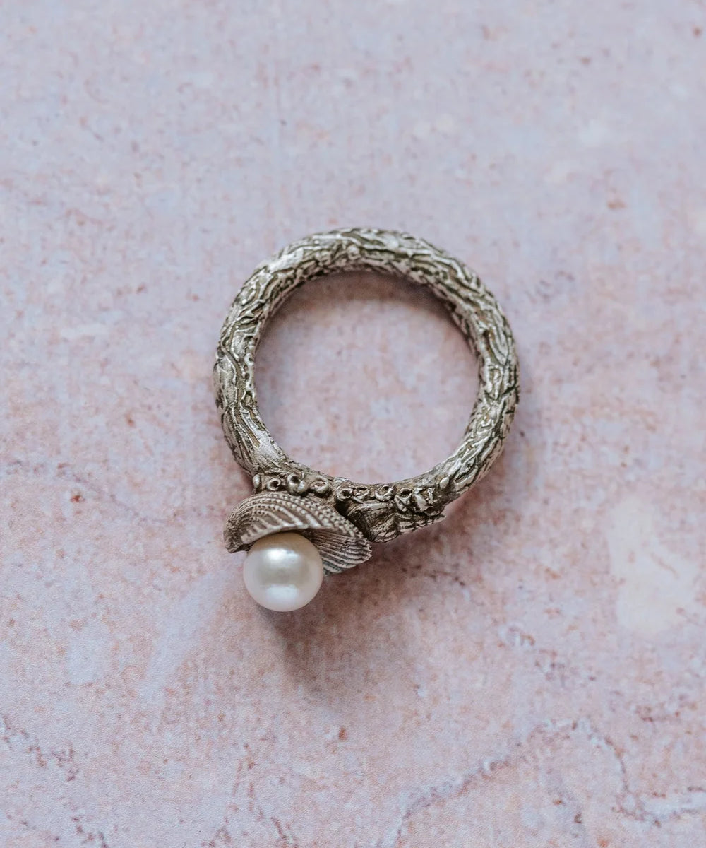 Handmade recycled silver ring with textured band and freshwater pearl in shell setting, on textured stone background