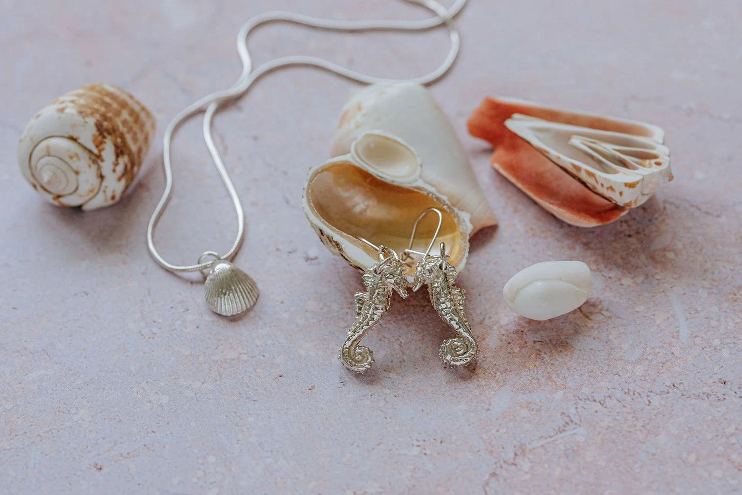 Handcrafted silver seahorse earrings and shell pendant necklace styled with natural seashells, part of a coastal inspired jewellery collection.