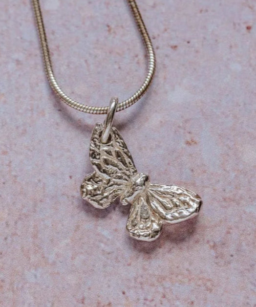 Handmade recycled silver small butterfly pendant on 18-inch snake chain, displayed on textured stone background