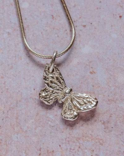 Handmade recycled silver small butterfly pendant on 18-inch snake chain, displayed on textured stone background