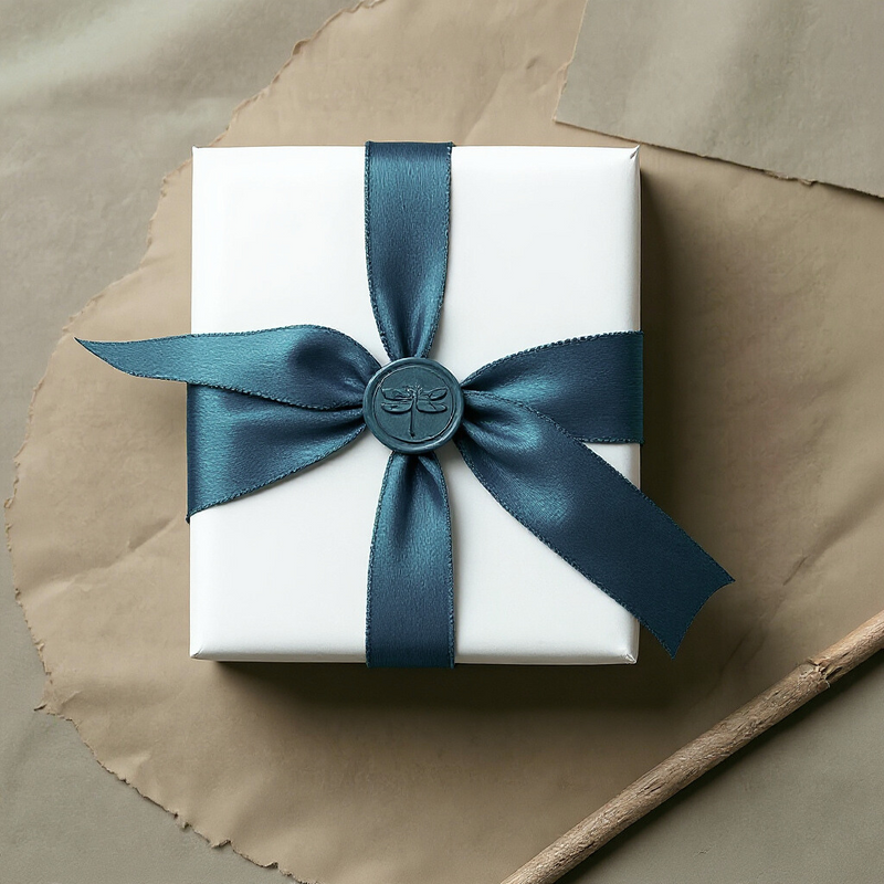 Elegant white jewellery gift box with teal satin ribbon and wax seal featuring dragonfly design, showcasing luxury packaging for handmade silver jewellery.