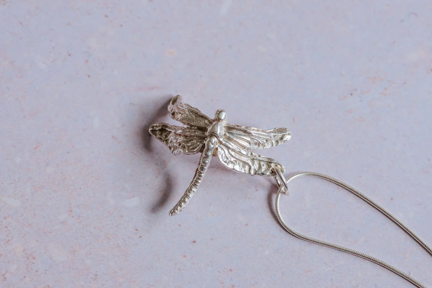 Handmade silver dragonfly necklace displayed flat with sterling silver snake chain, nature inspired artisan jewellery
